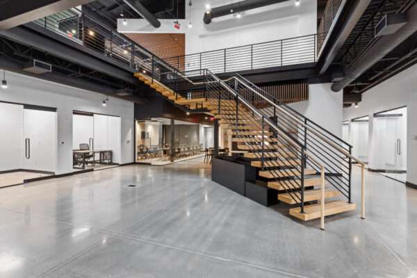 Modern office with open space, glass rooms, and wood staircase.