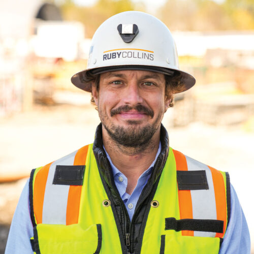 Man in RUBY COLLINS hard hat and vest at construction site.