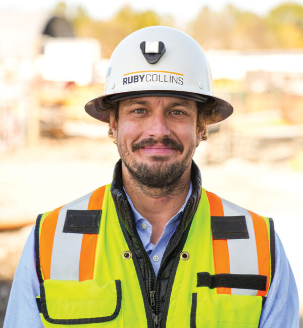 Man in RUBY COLLINS hard hat and vest at construction site.