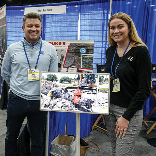 Two people at a trade show booth with construction display.