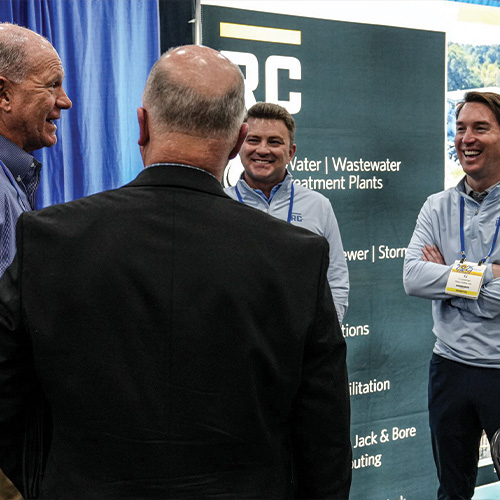 Four men smile at a trade show booth.