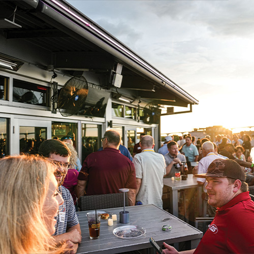 People socialize on a rooftop patio at sunset with drinks.