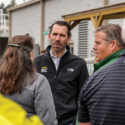 Man in RC jacket talks with two people outdoors.