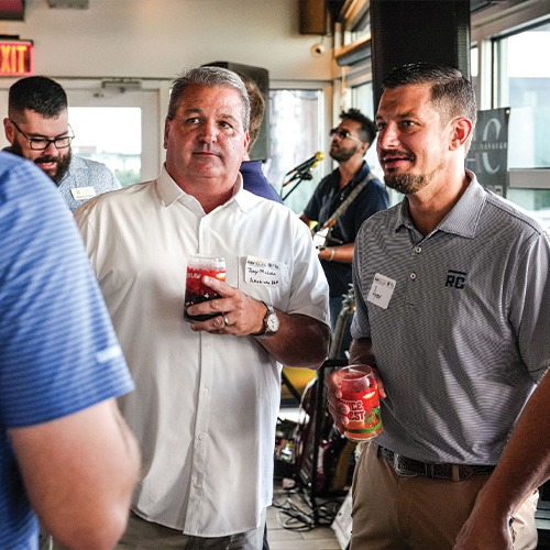 Two men with drinks and name tags at indoor gathering.