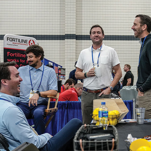 Four men converse at a trade show booth with banners.