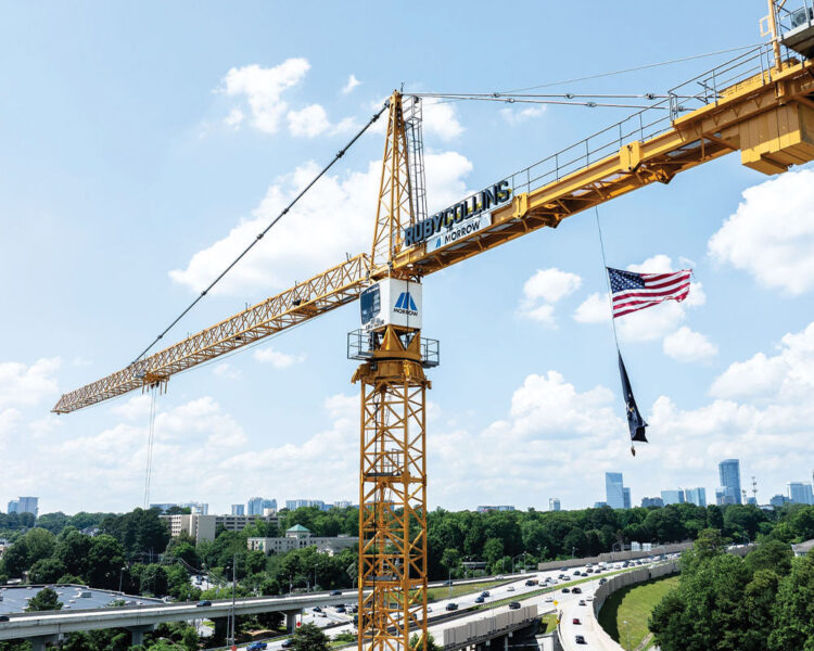 Yellow crane with American flag above highway, city in background.