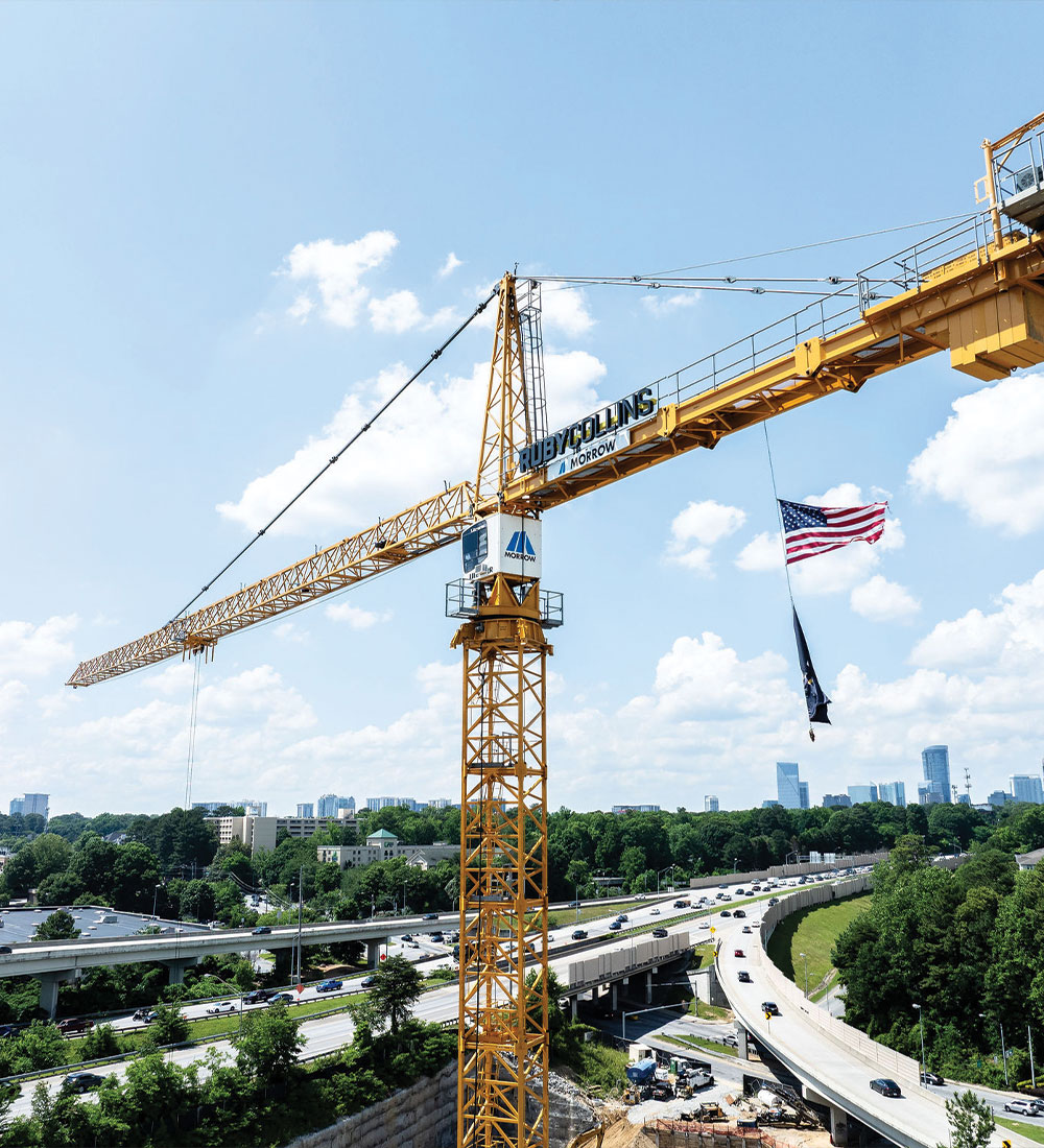Yellow crane with American flag above highway, city in background.
