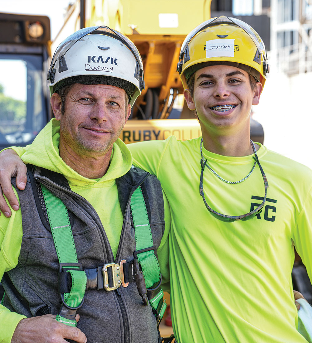 Two smiling construction workers in safety gear stand together.