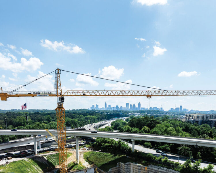 Crane over busy highway, city skyline and clouds behind.