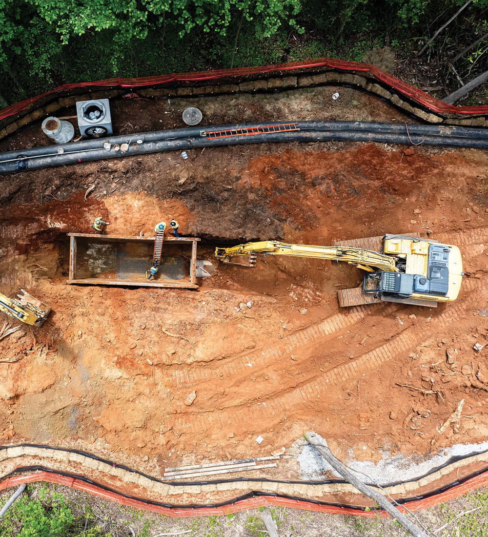 Aerial shot of excavator and workers digging trench among pipes.