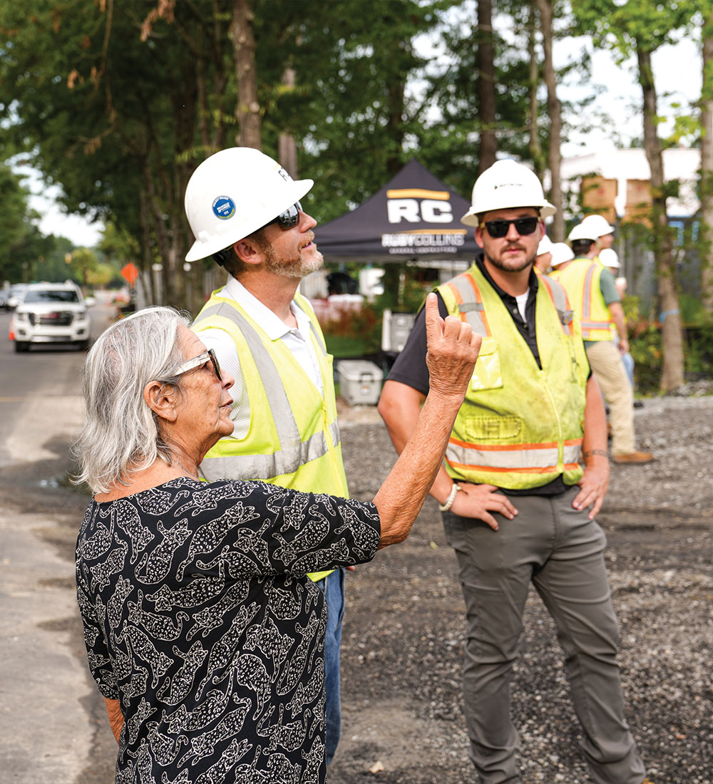 Older woman gestures to three construction workers at roadside.