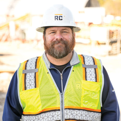 Construction worker in hard hat and vest at a site.
