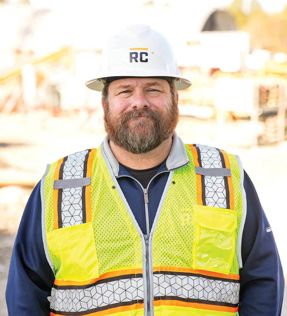 Construction worker in hard hat and vest at a site.