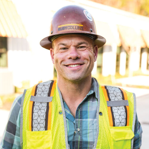 Smiling worker in RUBY COLLINS hard hat and vest outside.