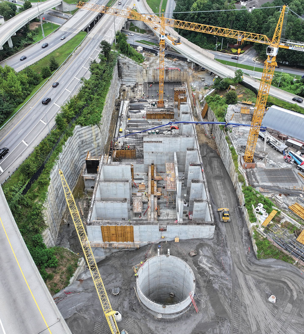 Construction site with cranes, circular foundation, highways nearby.