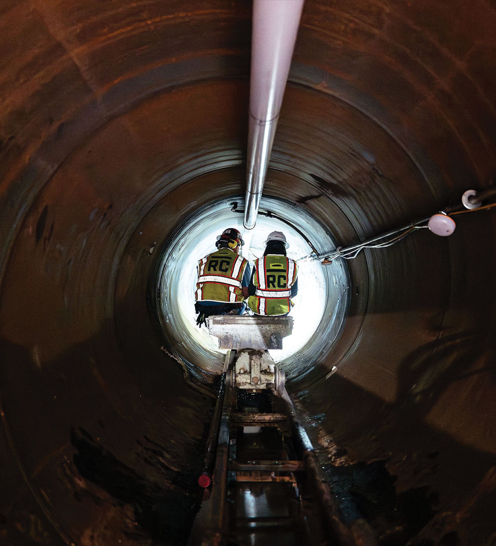Two workers in vests sit in a lit underground tunnel.