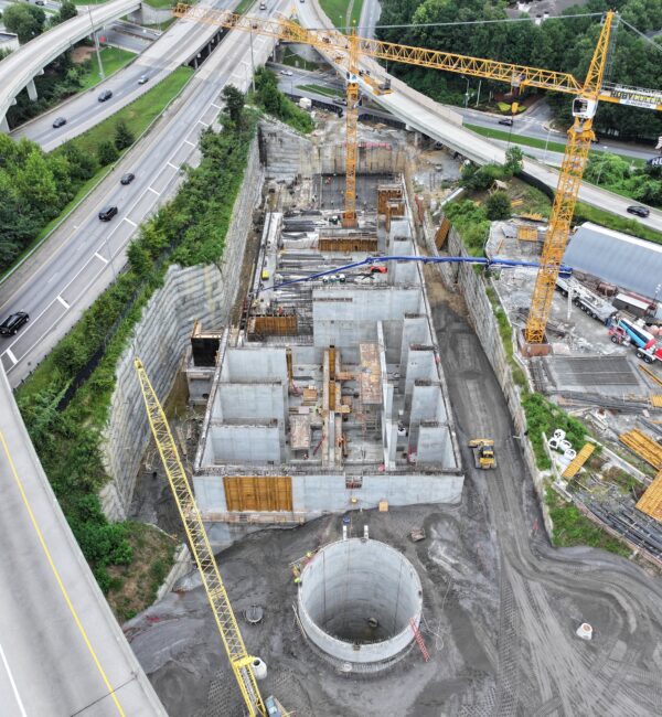 Aerial of construction site with cranes, highways, concrete, circular pit.