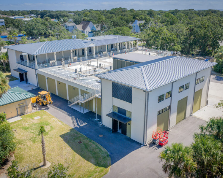 Aerial view of modern industrial building with metal roof, trees.