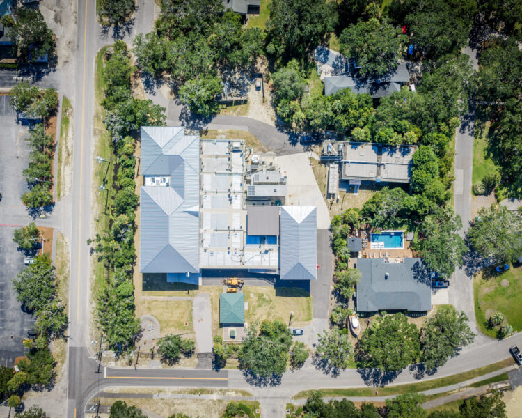 Aerial view of building complex, trees, roads, cars, homes, pool.