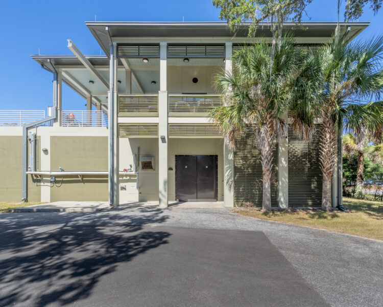 Green two-story building, flat roof, outdoor stairs, palm trees.