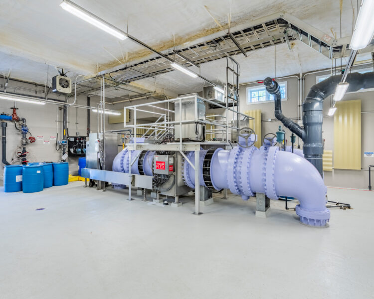 Industrial water filtration system with pipes, valves, and blue barrels.