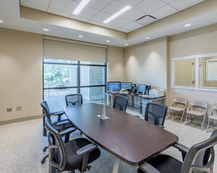 Conference room with long table, chairs, computers, and large windows.