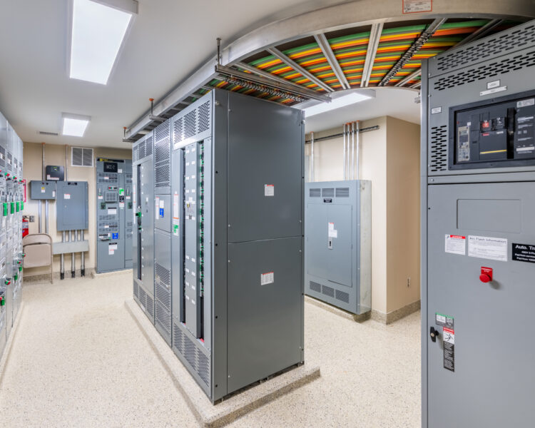 Room with electrical panels, circuit breakers, and overhead wiring trays.