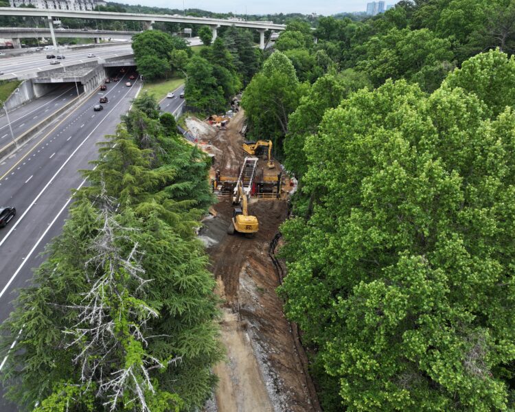 Construction site and workers by highway, surrounded by trees.