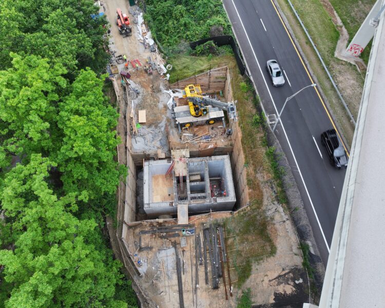 Aerial shot: construction site, machinery, materials, highway, trees, vehicles.