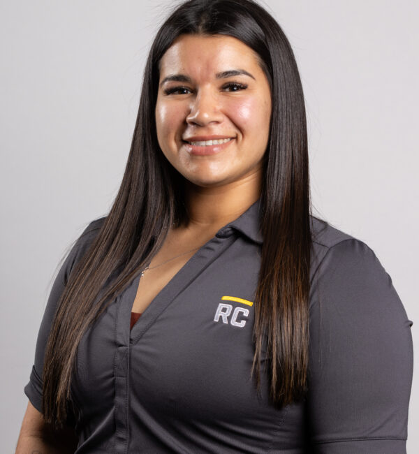 Smiling woman with long hair in RC shirt against plain background.