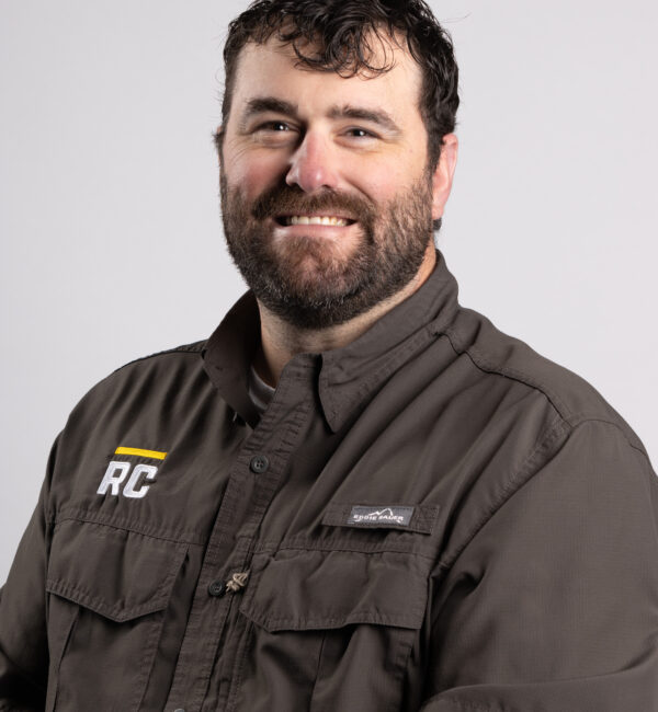 Bearded man in gray shirt smiling against a plain background.
