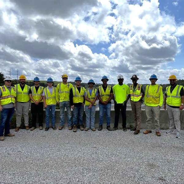 People in safety vests and hard hats stand outdoors in a line.