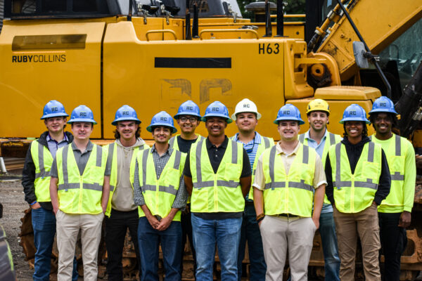 Once trabajadores con chalecos y cascos junto a un vehículo amarillo.