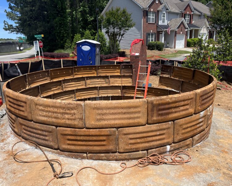 Estructura circular de hormigón con paneles marrones y una escalera roja cerca.