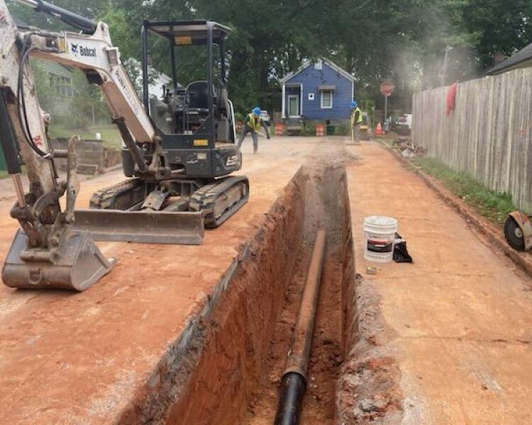 Un equipo instala una tubería de gran tamaño en una zanja con una excavadora cerca.