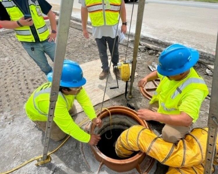 Four workers at roadside manhole; two work, two observe.