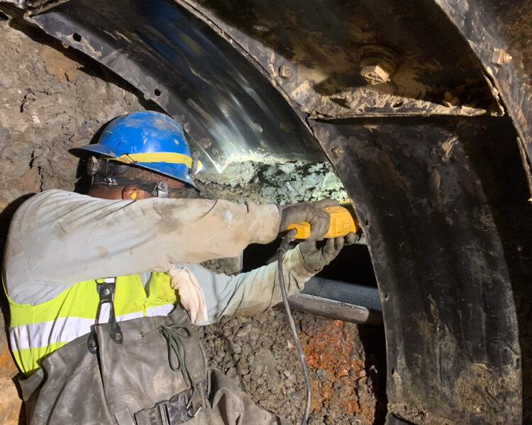 Un trabajador equipado con material de seguridad fija una pieza metálica en un túnel con una herramienta eléctrica.