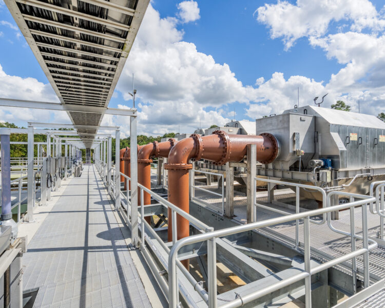 Pasarela de una instalación industrial con tuberías y equipos bajo las nubes.