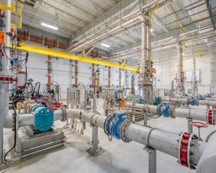 Nave industrial con tuberías, bombas y conductos a la vista en el techo.