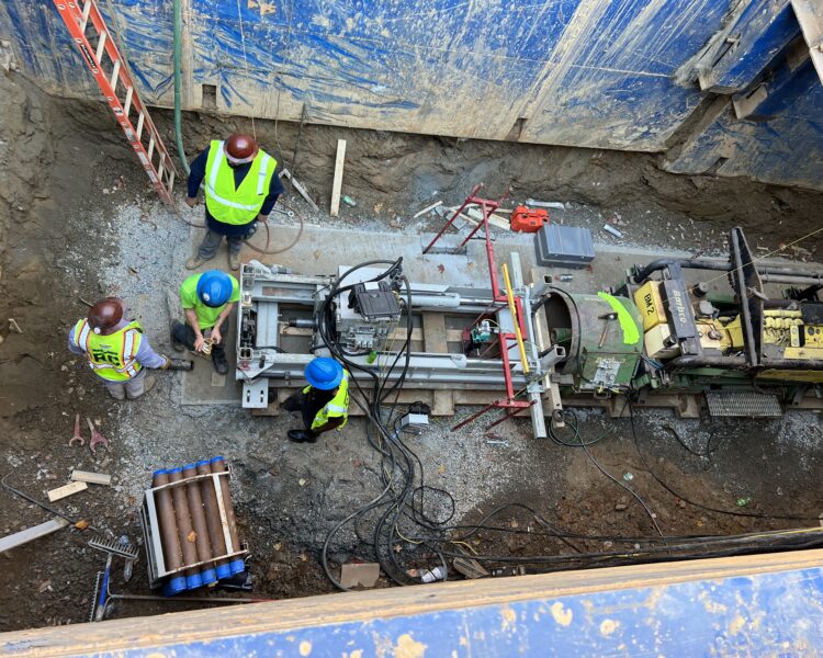 Cuatro obreros de la construcción con equipo de seguridad en una obra de excavación profunda.