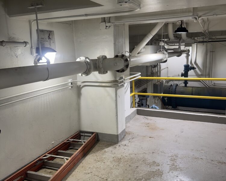 Industrial space with pipes, red ladder, yellow rails, white walls.