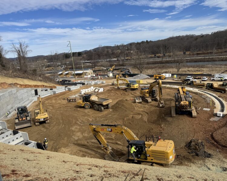 Construction vehicles and workers at a dirt site with retaining walls.