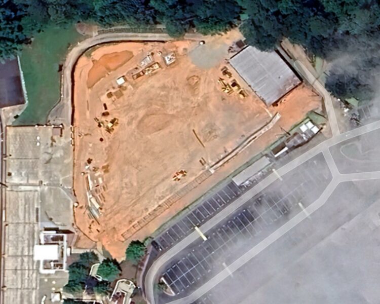 Construction site beside stadium, parking lot, and trees.