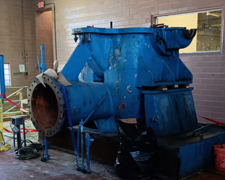 Rusty blue industrial pump amid tiles, caution tape, trash bag.
