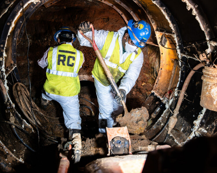 Dos trabajadores con equipo de seguridad retiran escombros con palas en el interior de un túnel.