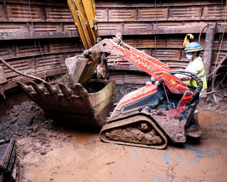 Un trabajador utiliza una excavadora llena de barro en una obra circular y cerrada de tierra.