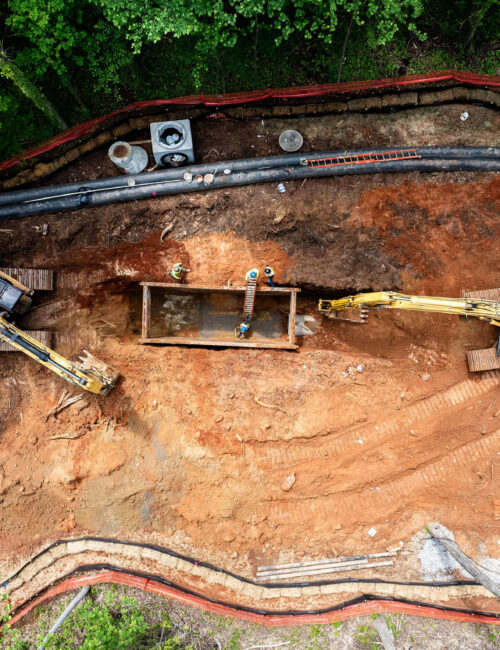 Excavators and workers installing pipes at a dirt construction site.