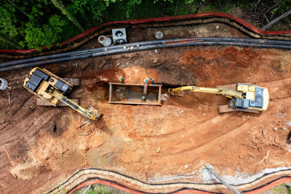Excavadoras y trabajadores instalando tuberías en una obra sin asfaltar.