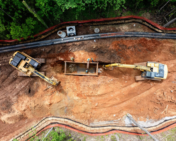 Excavadoras y trabajadores instalando tuberías en una obra sin asfaltar.