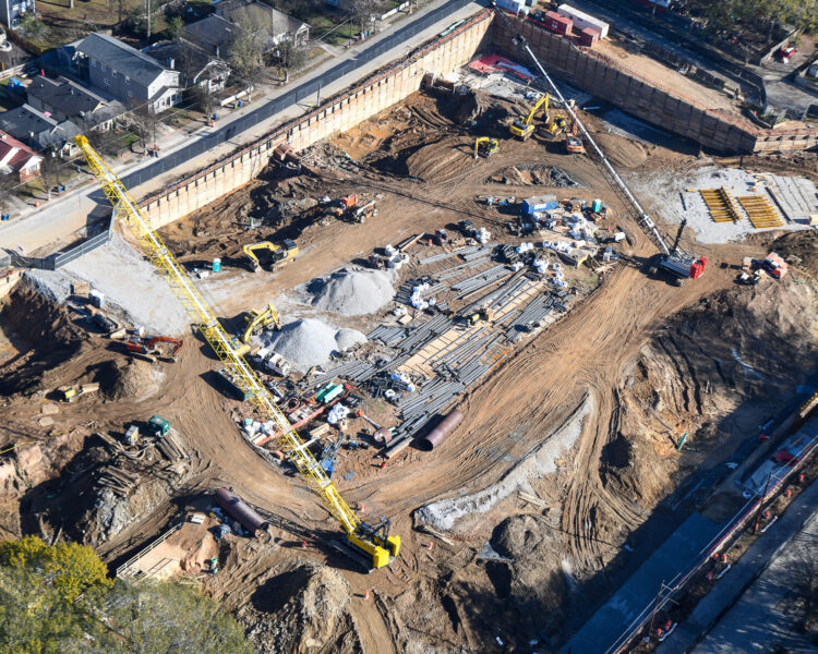 Aerial view: construction site with cranes, nearby roads and houses.